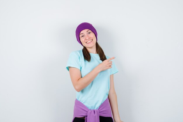 Maravillosa dama apuntando hacia el lado derecho con blusa, gorro y mirando alegre, vista frontal.