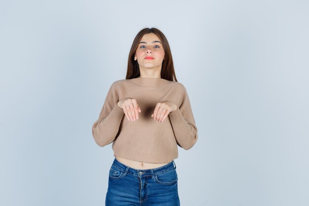 Maravillosa dama manteniendo las manos como patas en suéter, jeans y con un aspecto divertido, vista frontal.