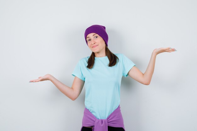 Maravillosa dama mostrando un gesto de impotencia en blusa, gorro y mirando vacilante, vista frontal.