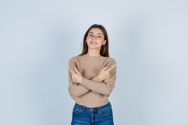 Maravillosa dama en suéter, jeans apuntando hacia arriba mientras sonríe y mira alegre, vista frontal.