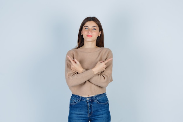 Maravillosa dama en suéter, jeans apuntando hacia los lados izquierdo y derecho y luciendo complacida, vista frontal.