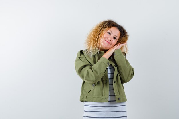 Maravillosa mujer en chaqueta verde, camisa apoyada en la mejilla en las manos y mirando optimista, vista frontal.