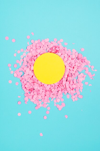 Marco en blanco amarillo sobre el confeti rosado circular festivo pequeño contra el fondo azul