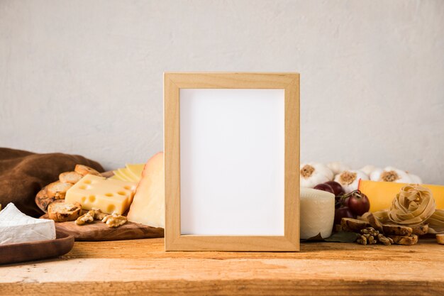 Marco en blanco delante de queso e ingrediente en mesa de madera