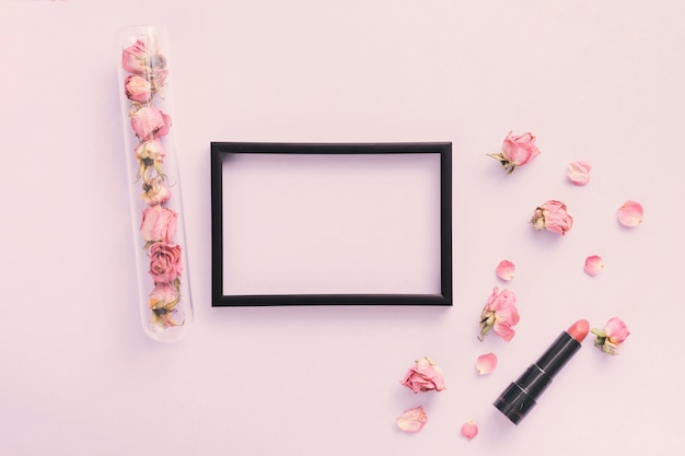 Foto gratuita marco en blanco con pétalos de rosa y lápiz labial en la mesa