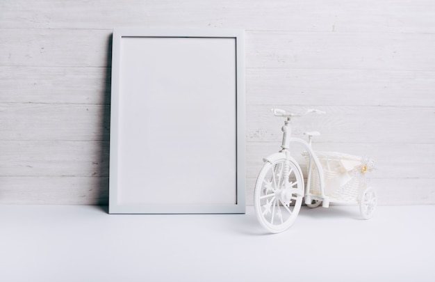 Un marco blanco vacío cerca de la bicicleta en el escritorio blanco contra la pared de madera