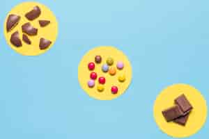 Foto gratuita marco circular amarillo sobre los caramelos de gemas de colores; cáscaras de huevo de pascua y trozos de chocolate sobre fondo azul