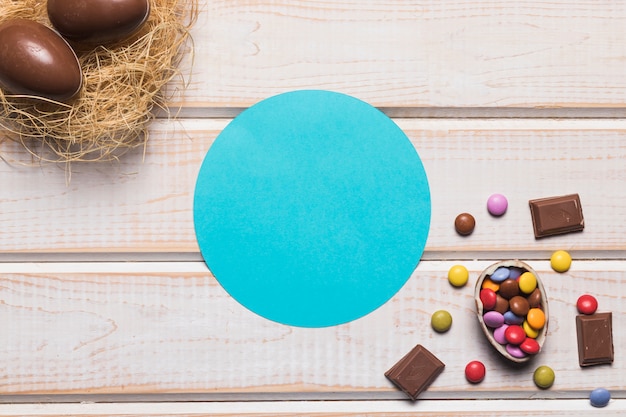 Marco circular azul con chocolates y huevos de Pascua en el nido sobre el escritorio de madera