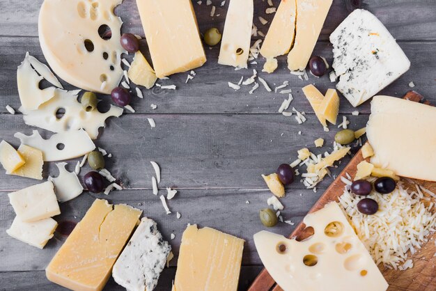 Marco circular hecho con diferentes tipos de queso y aceitunas en mesa de madera