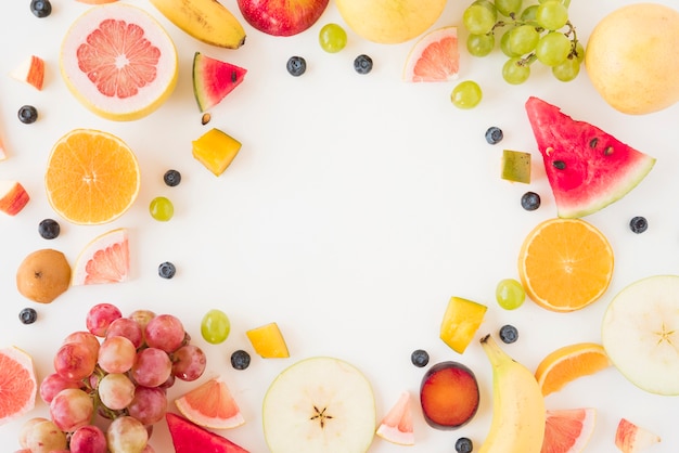 Marco circular hecho con muchas frutas orgánicas sobre fondo blanco.