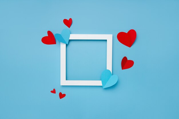 marco cuadrado blanco sobre fondo azul con corazones de papel