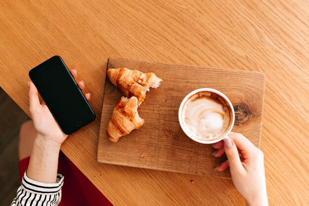 Marco encima de una taza de café con croissant sobre placa de madera.