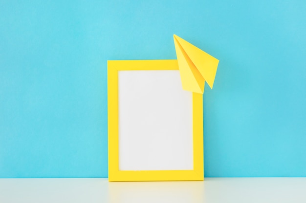 Marco de foto amarilla y avión de papel delante de la pared azul