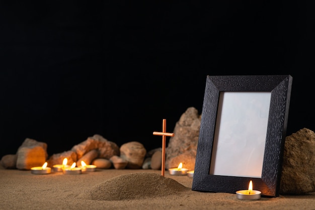 Marco de fotos con velas de piedras y pequeña tumba en la superficie oscura de arena