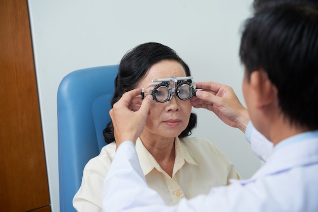 Marco de lente de prueba de ajuste oftalmólogo masculino irreconocible para paciente femenino senior