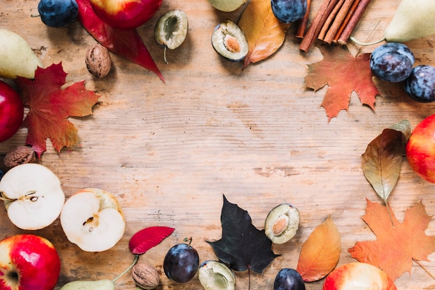 Marco de otoño con hojas y frutas sobre fondo de madera