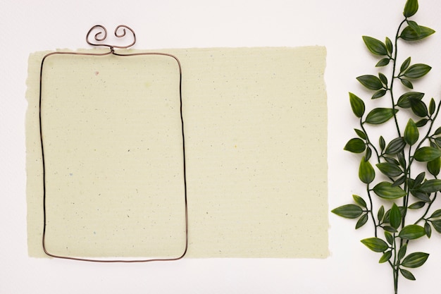 Foto gratuita marco rectangular vacío sobre papel cerca de las hojas verdes artificiales sobre fondo blanco