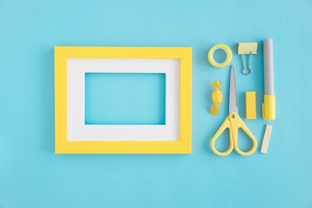 Foto gratuita un marco vacío con borde blanco y amarillo y papelería sobre fondo azul