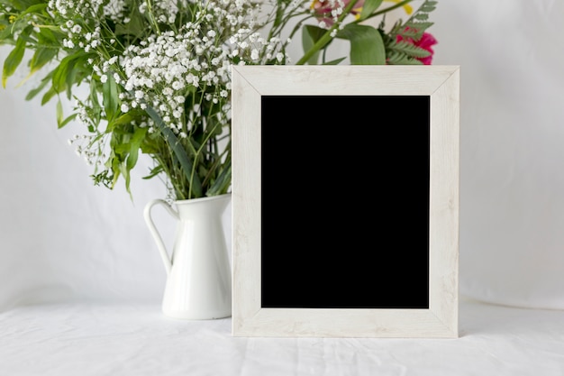 Marco vacío de la foto en blanco con el florero en la tabla blanca