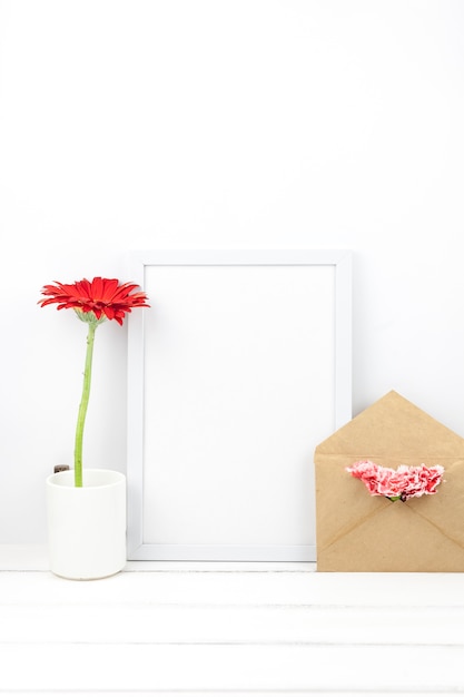 Marco vacío; vaso; Flores y sobre sobre mesa de madera.