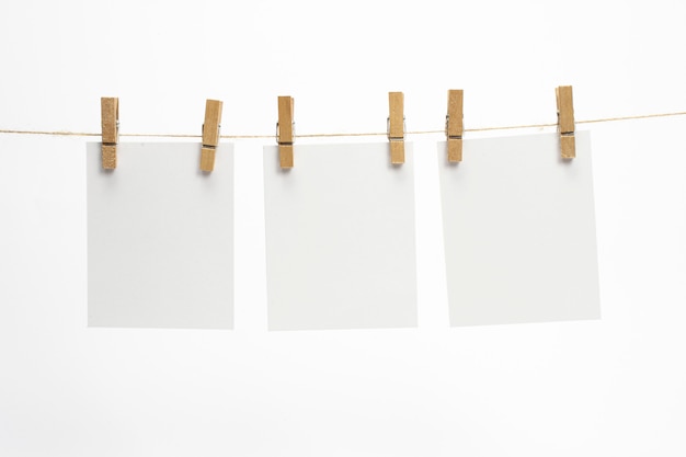 Marcos de papel vacíos que cuelgan de una cuerda con pinzas para la ropa y aislados en blanco. Tarjetas en blanco en la cuerda.