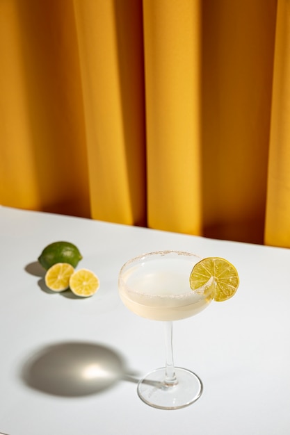 Margarita en vaso con limón en mesa blanca contra cortina amarilla
