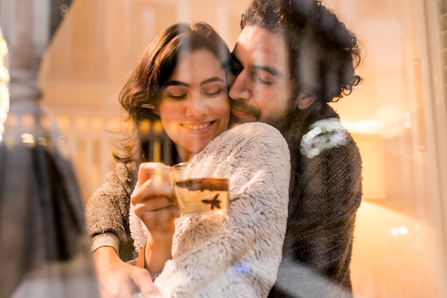 Marido abrazando a su esposa mientras ella sostiene una taza de té