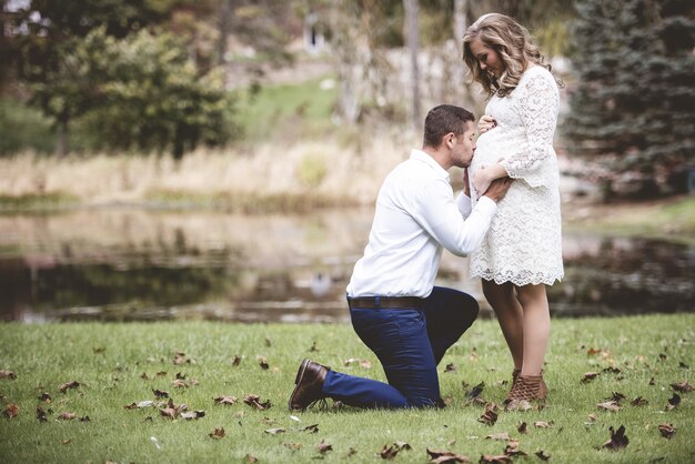 Marido besando el vientre de su esposa embarazada en un jardín con un lago