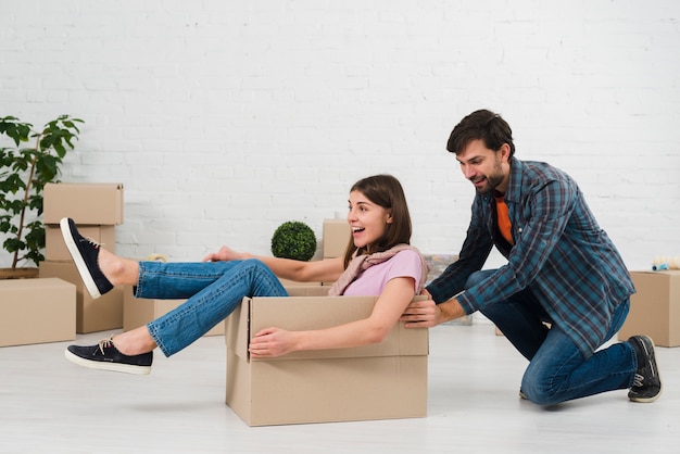 Marido empujando a su esposa sentada en la caja de cartón