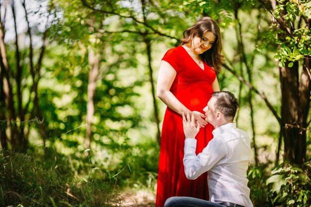 El marido con la esposa embarazada abrazando en el bosque
