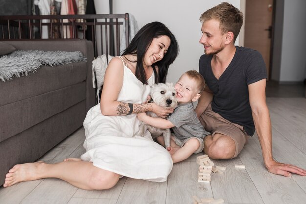 Marido mirando a su esposa jugando con un perro y sonriendo a su hijo en casa