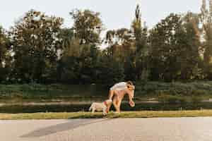 Foto gratuita marido y mujer jugando y bailando tango en el parque cerca del estanque mientras caminan con labrador.