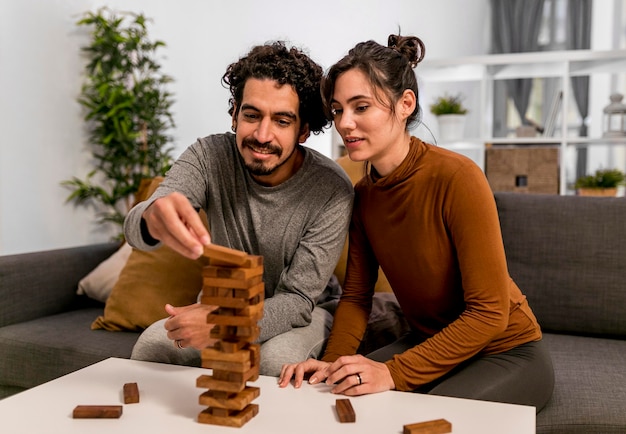 Marido y mujer jugando un juego de torre de madera en interiores