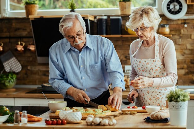 Marido y mujer maduros preparando bruschetta en su cocina