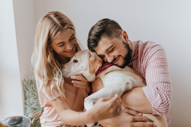 Foto gratuita marido y mujer positivos juegan con perro. hombre con camisa a rayas abraza a labrador con ternura.