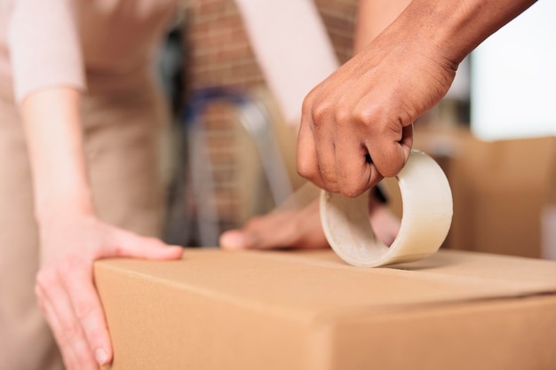 Marido y mujer usando cinta adhesiva para empacar cajas, usando embalaje de carga para envío y transporte en un nuevo apartamento alquilado. Rodillo adhesivo para mover en el hogar. De cerca.