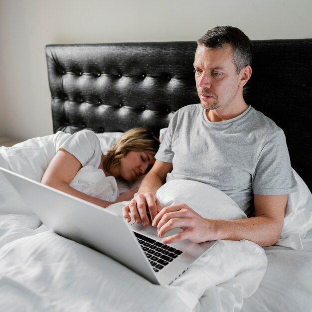 Marido con ordenador portátil mientras la esposa está dormida