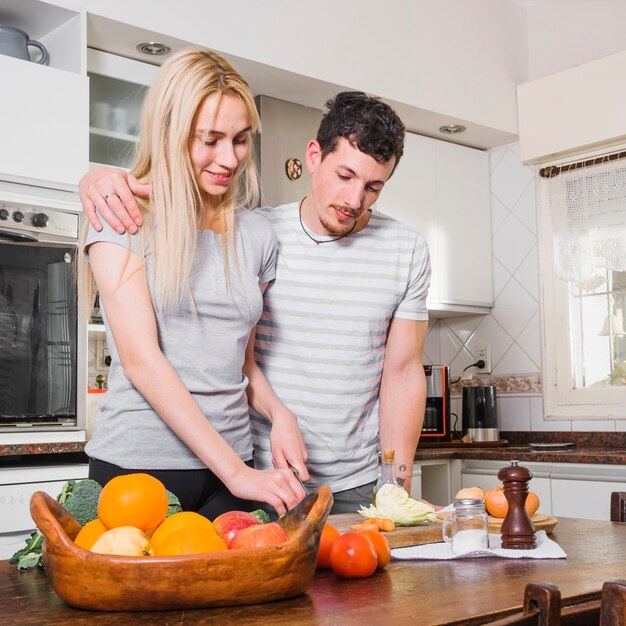 Marido de pie con su esposa cortando verduras en la mesa