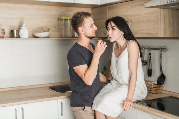 Marido sonriente alimentando comida a su esposa sentada en la cocina