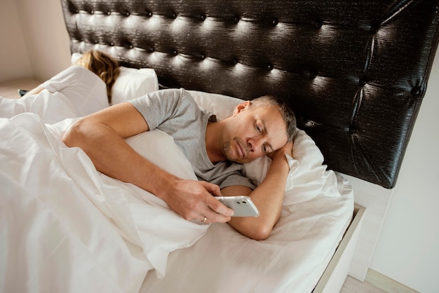 Marido usando el móvil mientras la esposa está durmiendo