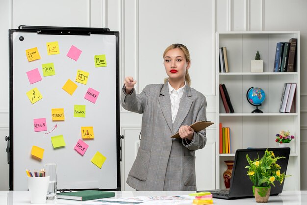 Marketing joven y linda mujer de negocios con chaqueta gris en la oficina señalando a un miembro del equipo
