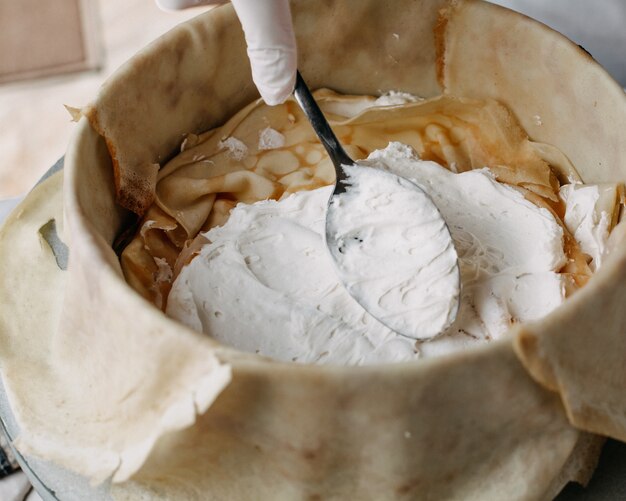 masa dentro de una sartén redonda con el cocinero esparciendo crema agria dentro de la cocina