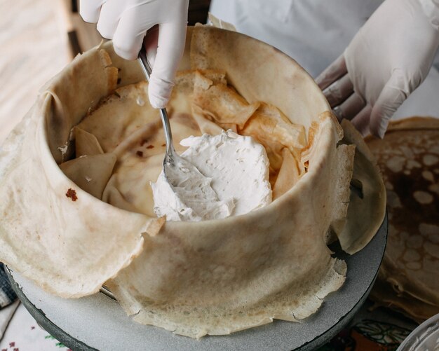 masa dentro de una sartén redonda con el cocinero esparciendo crema agria dentro de la cocina