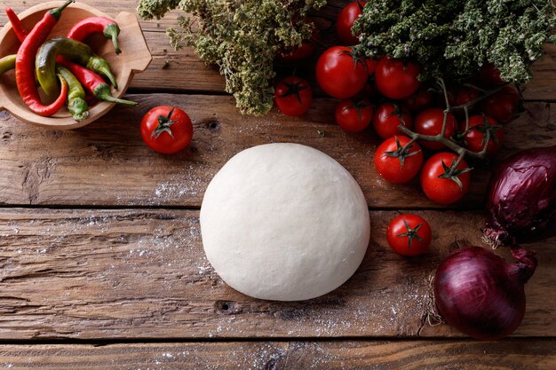 Masa de masa en una mesa de madera rodeada de tomates, pimientos y cebollas