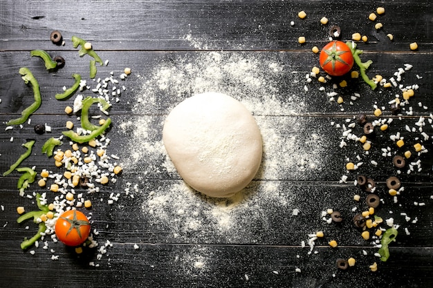 Masa de pizza espolvoreada con harina colocada al lado de queso espolvoreado de maíz de oliva tomate pimiento