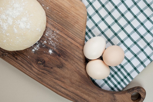 Masa con tres huevos blancos frescos de pollo sobre tabla de cortar de madera.