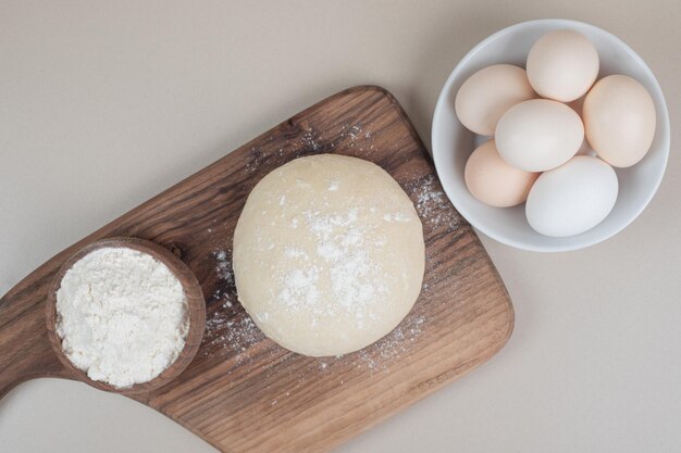 Masa con tres huevos blancos frescos de pollo sobre tabla de cortar de madera.