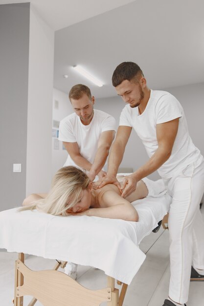 El masaje a cuatro manos. Concepto de salud y belleza femenina. Dos masajistas hacen un doble masaje a una chica. Mujer en un salón de spa.