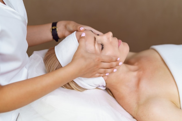 Masaje facial. Primer plano de mujer adulta recibiendo tratamiento de masaje spa en el salón de belleza spa. Spa para el cuidado de la piel y el cuerpo. Tratamiento de belleza facial. Cosmetología.