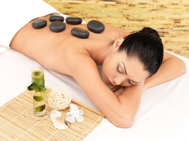 Masaje con piedras para mujer joven en el salón de belleza spa. Terapia de recreación.